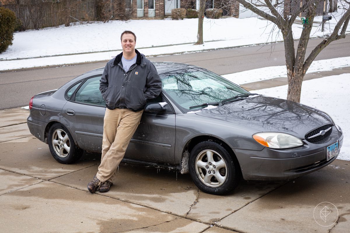 Charlie Hall standing leaning against a gray Ford Taurus in a driveway