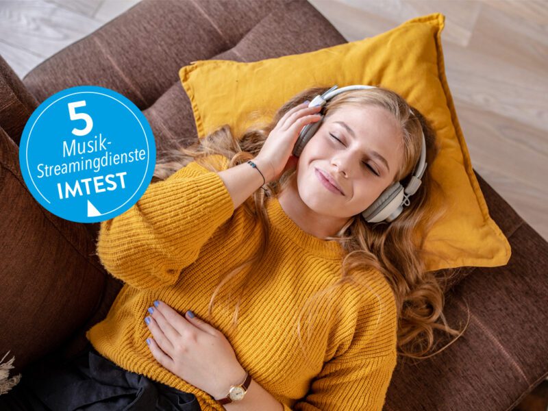 Smiling young woman lying on sofa wearing headphones